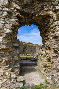 Ancient stone archway framing inner courtyard of a ruined castle. Close-up view of weathered masonry, rough textures, and mossy stone blocks.