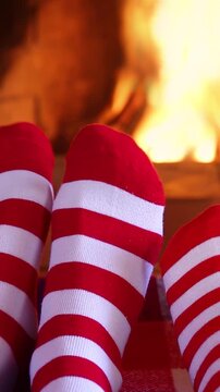 Feet dressed in wool socks with a Christmas ornament in front of the fireplace. The family is having fun at home on Christmas Eve. Vertical video