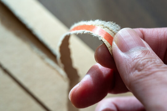 Hand Holding Torn Corrugated Cardboard Strip With Orange Line