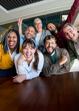 Vertical. Multicultural coworkers laughing during a lively office meeting, showcasing teamwork, friendship, success, and a vibrant corporate atmosphere.