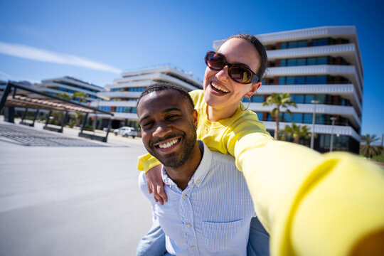 Happy couple share a fun piggyback pose outdoors in a sunny residential district, creating a lively lifestyle and relationship portrait.