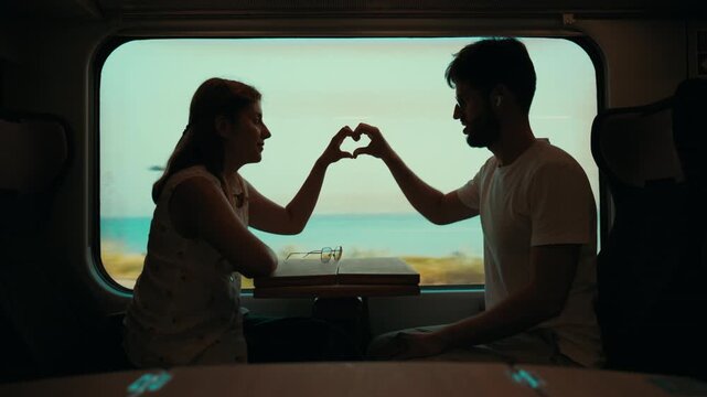 Silhouette of a couple make a heart shape of love while traveling on a train