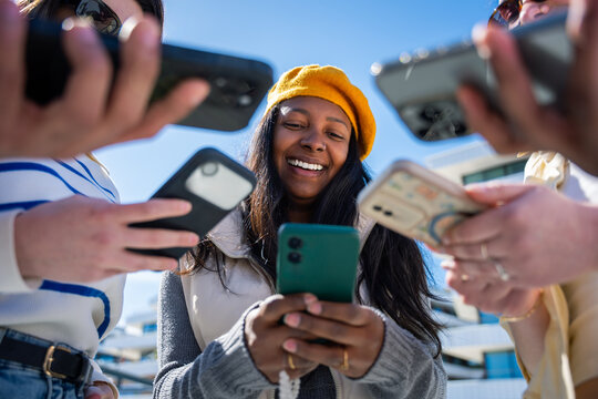 Outdoor lifestyle scene of a Black woman using a smartphone while surrounding hands hold phones and money, suggesting online payment and social finance.