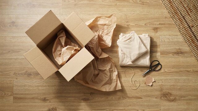 Open cardboard parcel box with kraft tissue paper scissors and twine on a light wooden table