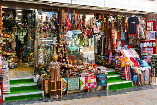 A traditional marketplace shop brimming with vibrant local products, intricately patterned textiles, handmade souvenirs, and hanging lanterns inside the historic Mutrah Souq in Muscat, Oman.