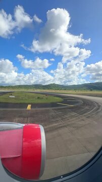 Airplane wing and engine view from window during taxiing on runway with blue sky and clouds in the background. 4K vertical footage