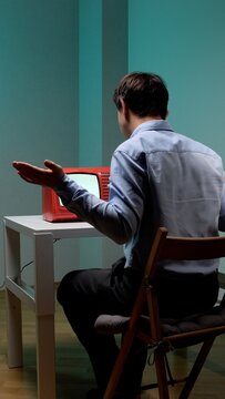 Man seen from behind shrugging in frustration at a small vintage red tv with a blank screen on a white table, symbolizing outdated technology and communication breakdown