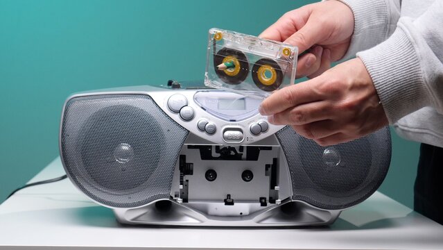 Hands inserting a clear cassette into a retro boombox tape deck, evoking nostalgic 80s90s music memories and analogue listening on a portable vintage stereo device