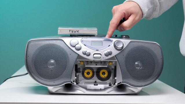 Hand pressing play button on a silver boombox, inserting a cassette tape labeled punk to listen to music, capturing moments of retro sound and nostalgia
