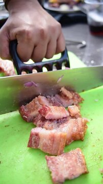 Close up of hands slicing freshly roasted crispy pork belly chicharron on a cutting board