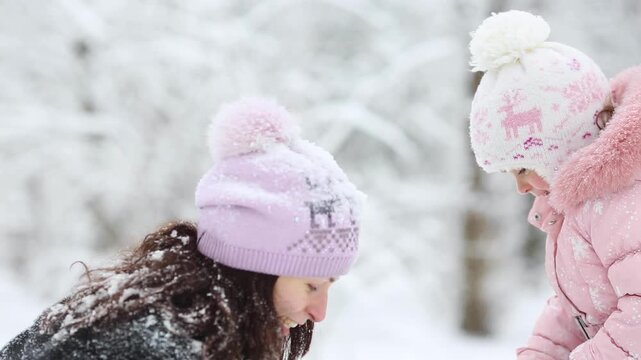 Mother and child are having fun outdoors in winter forest. A family plays in a nature park against a snow covered trees background. Slow motion