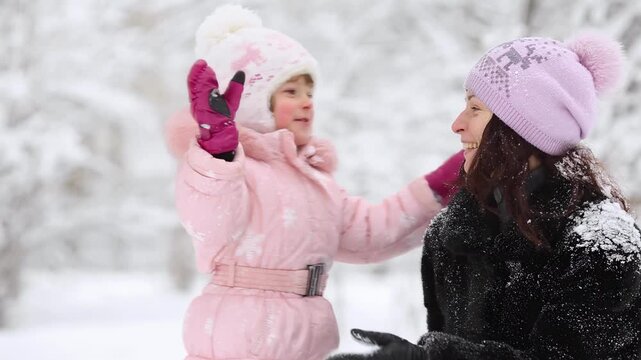 Mother and child are having fun outdoors in winter forest. A family plays in a nature park against a snow covered trees background. Slow motion