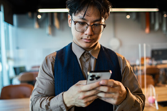 Young professional with glasses using smartphone in modern coworking office