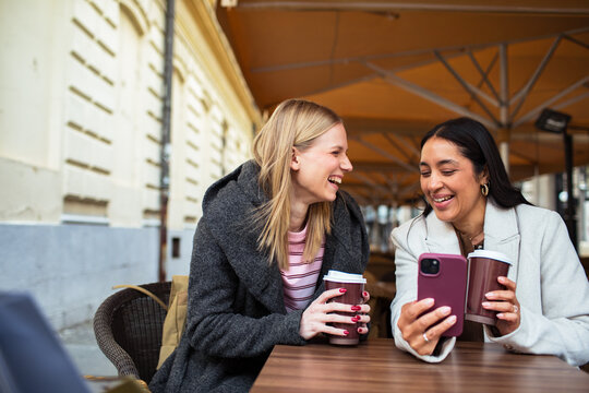 Two women friends laughing over coffee at outdoor cafe