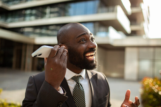 Cheerful businessman talking on smartphone outside office building
