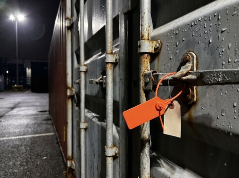 Orange security seal on rusty shipping container latch at night