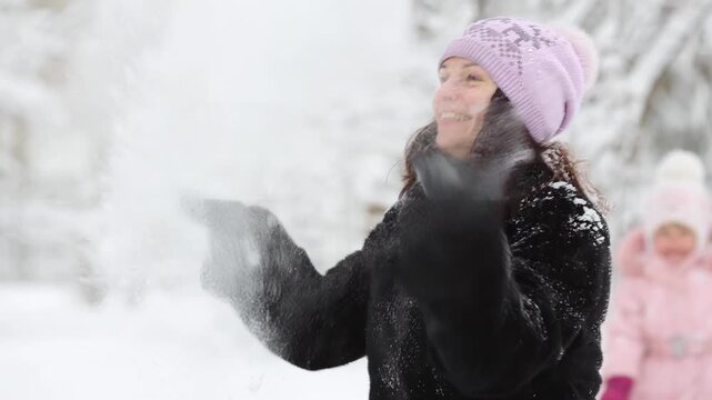 Mother and child are having fun outdoors in winter forest. A family plays in a nature park against a snow covered trees background. Slow motion