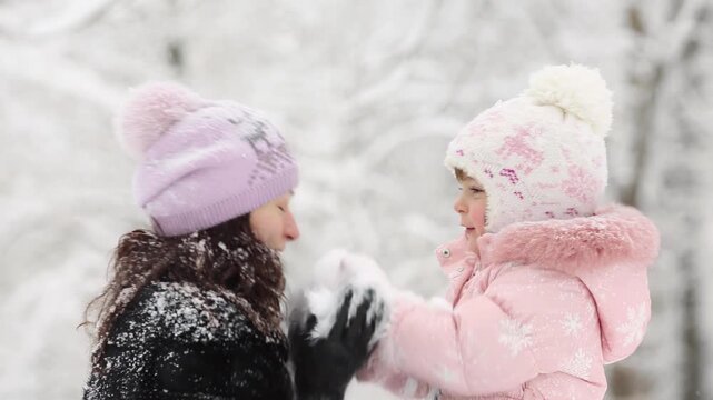 Mother and child are having fun outdoors in winter forest. A family plays in a nature park against a snow covered trees background. Slow motion