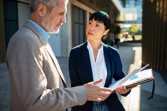 Two business professionals discussing financial report outside office building