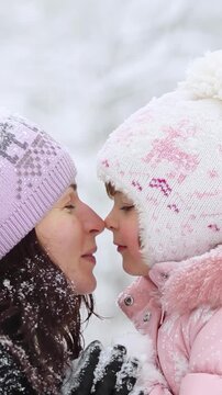 Mother and child are having fun outdoors in winter forest. A family plays in a nature park against a snow covered trees background. Slow motion. Vertical video