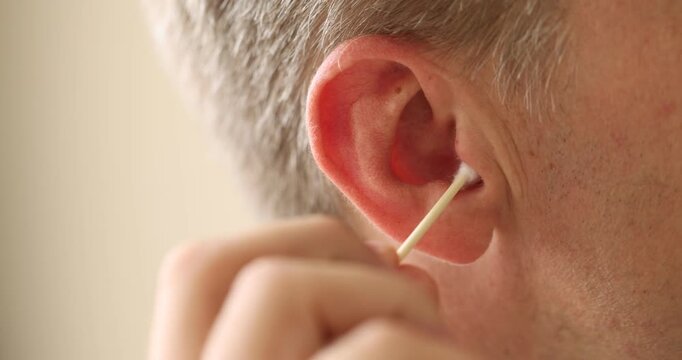 Man cleaning ear with cotton swab indoors, closeup