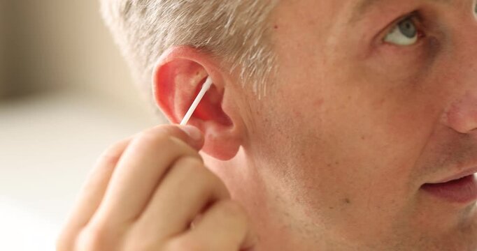 Man cleaning ear with cotton swab indoors, closeup