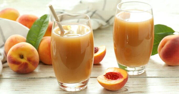 Glasses of tasty juice and peaches on wooden table, closeup. Camera moving right