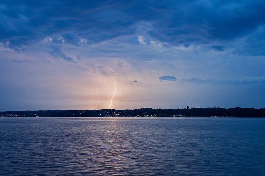 Lightning striking over calm water with cloudy blue sky at dusk in flensburg