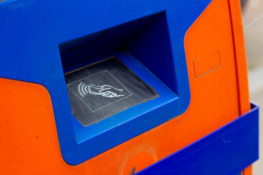 Horizontal street photo. Blue and orange ATM machine with contactless reader panel, plastic card icon. Concept of cash money, salary, credit, loan, debt, pay tax, buy, wages, budget, debit
