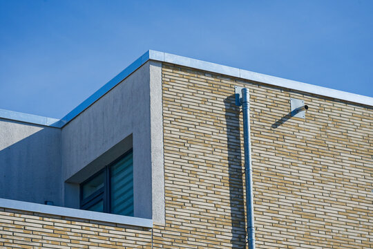 Modern building corner with brick wall and metal pipe under clear blue sky
