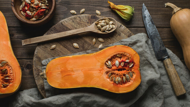 Fresh butternut squash cut in half with seeds and other kitchen items on wooden background.