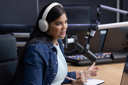 African American woman speaking into boom mic in studio with white headset, denim jacket at console