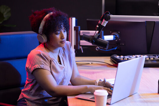 African American woman wearing headphones, recording podcast using laptop and broadcast microphone