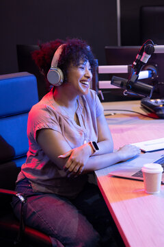 African American woman sitting at podcast studio desk wearing headphones and using microphone