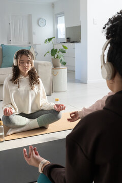 African American female family meditating together on tan yoga mat wearing headphones at home