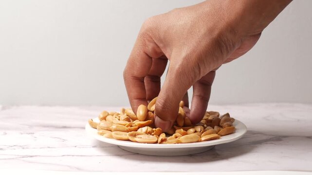 Hand picking roasted peanuts from white plate for snacking