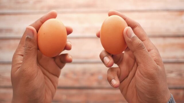 Two hands holding brown chicken eggs, comparing them with natural lighting in a close-up overhead shot, dynamic food preparation concept