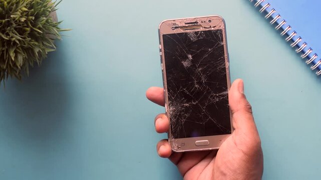 Close up view of person hand holding a smart phone with cracked screen on blue background