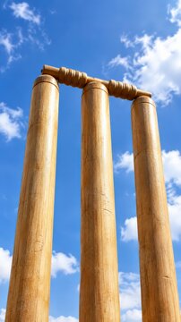 Close-up view of three cricket stumps with bails set on a bright day against a clear blue sky