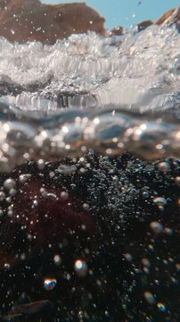 Transition from air to water: lens descends into surging torrent of white water. Below surface, an endless parade of bubbles dances in current&mdash;slow-motion study of power within mountain brook