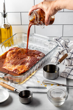 A hand pouring a freshly made spicy marinade onto a flank steak.
