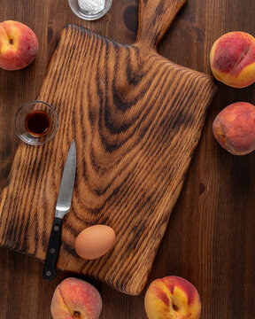 A wooden cutting board with peaches, a knife and other ingredients all around.