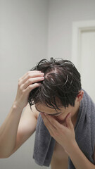Fototapeta premium Worried Japanese Young Man Checking Visible Scalp Through Wet Hair After Bath, Hair Loss Concern, Copy space on the top