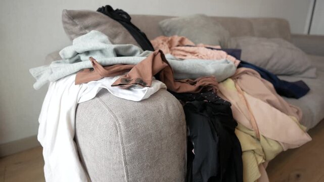 Messy clothes piled on sofa in bright room creating cluttered and disorganized scene with various fabric textures and colors