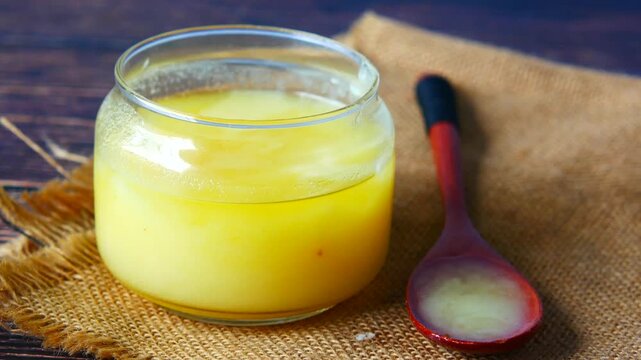 Clear liquid homemade ghee in glass jar and wooden spoon on burlap napkin
