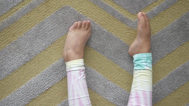 A close up view of a small child's legs and feet wiggling on a patterned carpet, capturing playful movement