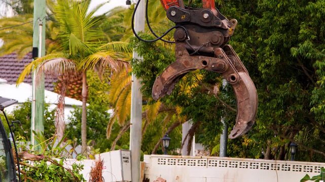 Demolition excavator grips tree roots for removal on construction site.