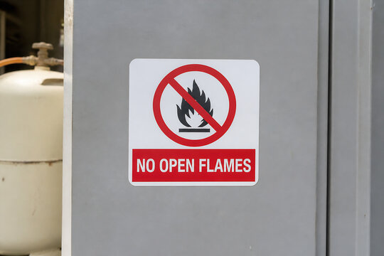 A "NO OPEN FLAMES" warning sign is displayed on a gray industrial cabinet next to a white tank.