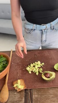 Mid adult millennial woman preparing a healthy green salad at home while drinking wine, dancing and singing, enjoying a relaxed and playful moment during everyday cooking.