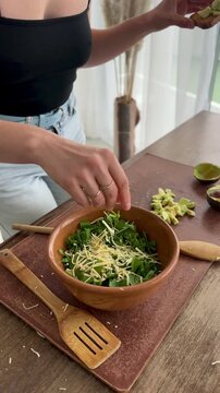 Mid adult millennial woman preparing a healthy green salad at home while drinking wine, dancing and singing, enjoying a relaxed and playful moment during everyday cooking.